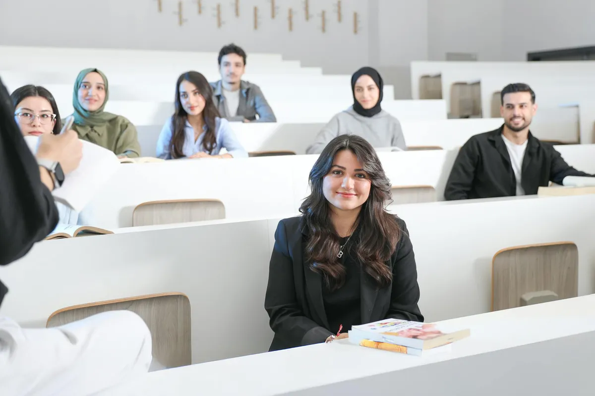 Estudante assistindo aula em sala de pós-graduação como ouvinte, caderno na mão
