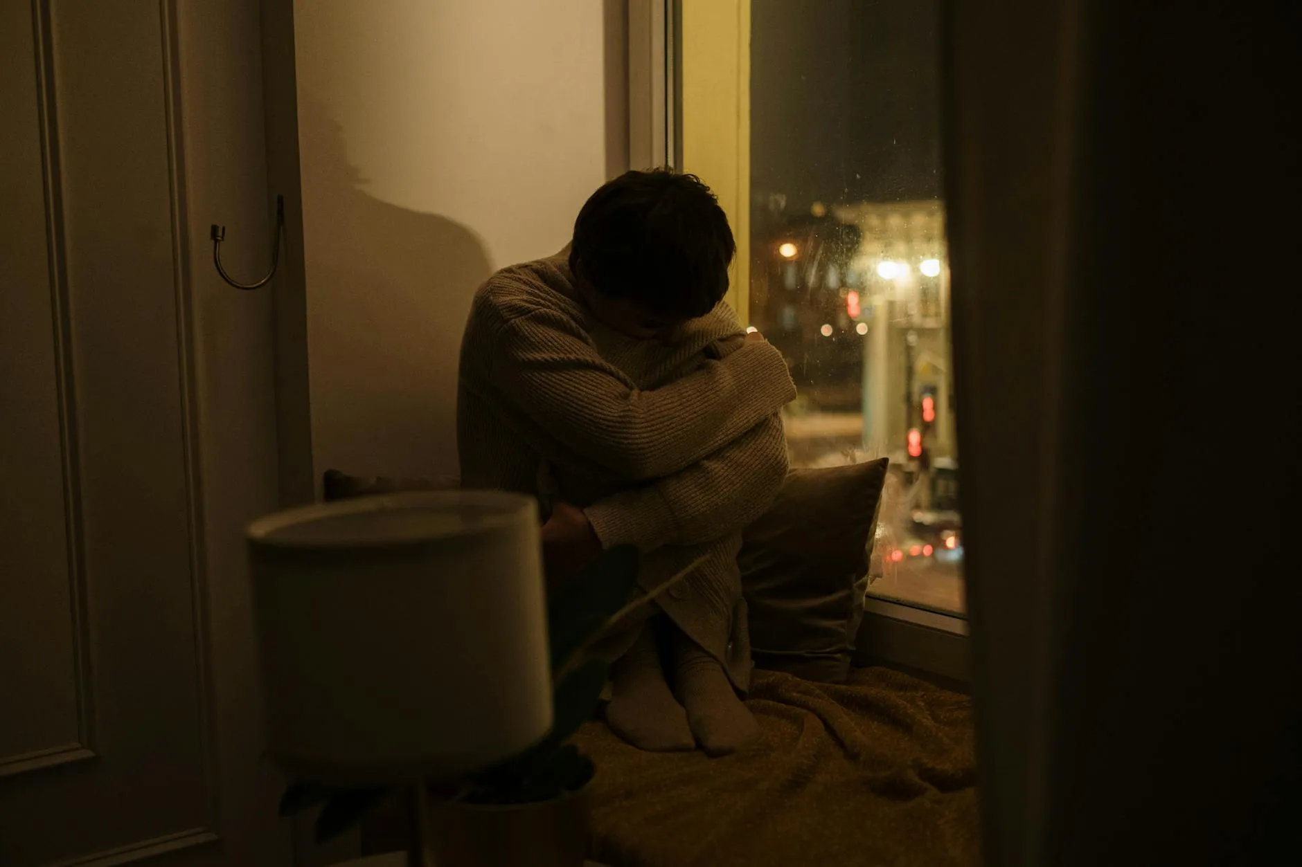 Pessoa sentada abraçando os joelhos com expressão pensativa em ambiente tranquilo