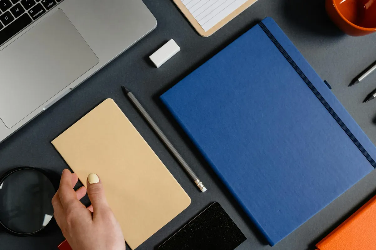 Mesa organizada com blocos de texto manuscrito e computador, representando escrita em lote