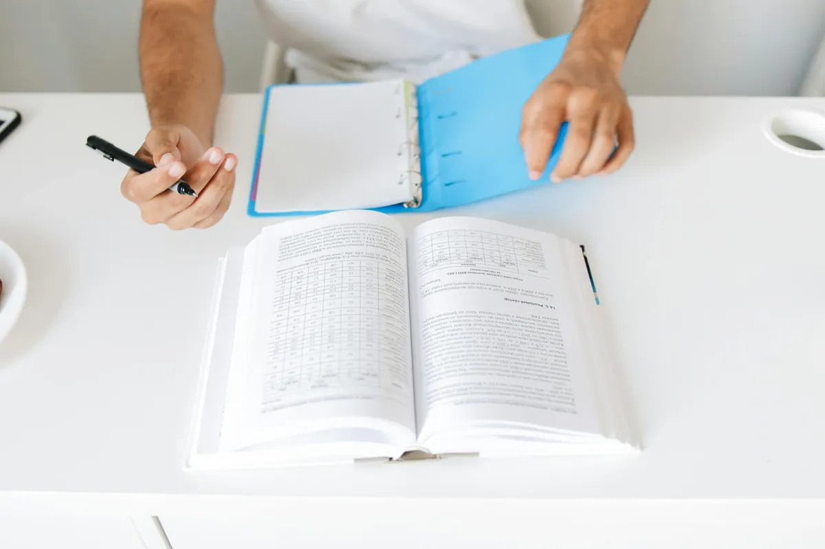 Livros abertos sobre mesa com caderno de anotações e caneta