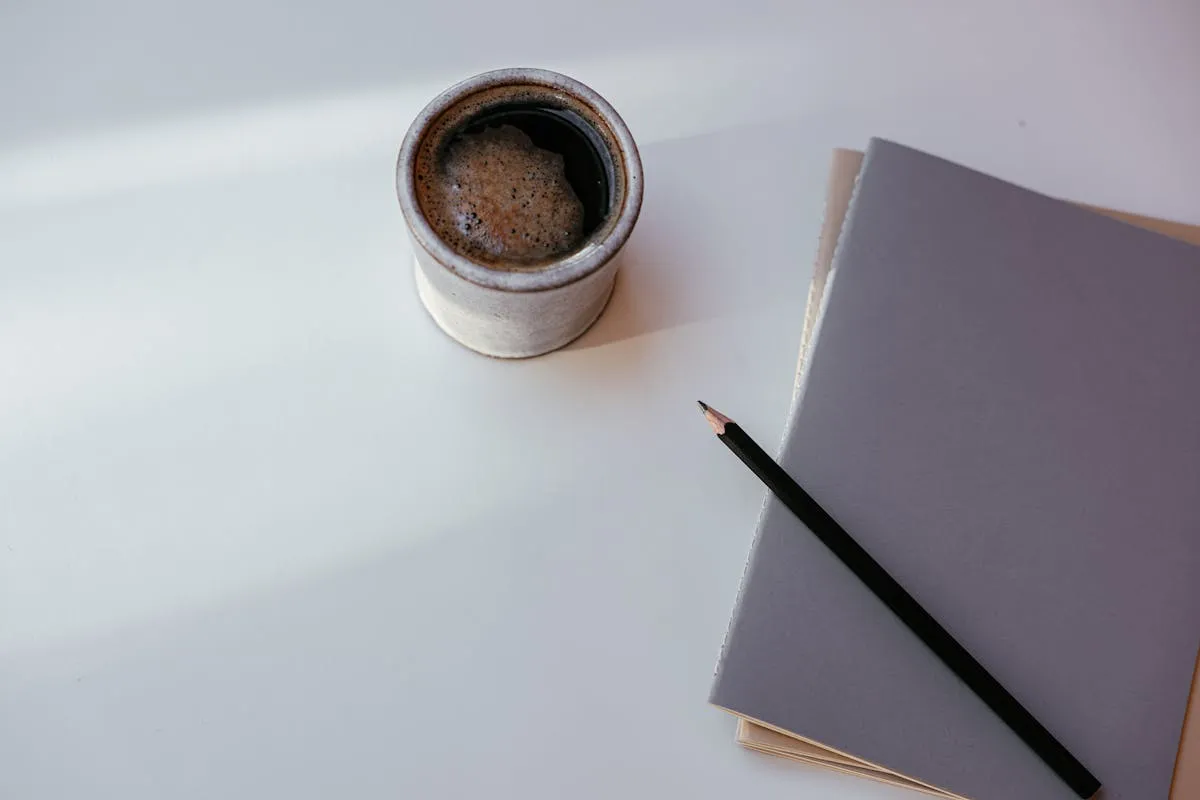 Mesa de trabalho organizada com caderno, computador e xícara de café - ambiente de escrita acadêmica