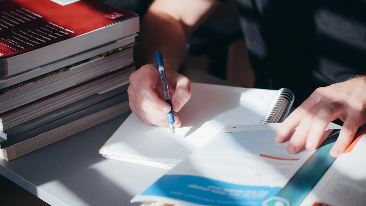 Pesquisadora escrevendo em caderno ao lado de artigos científicos impressos