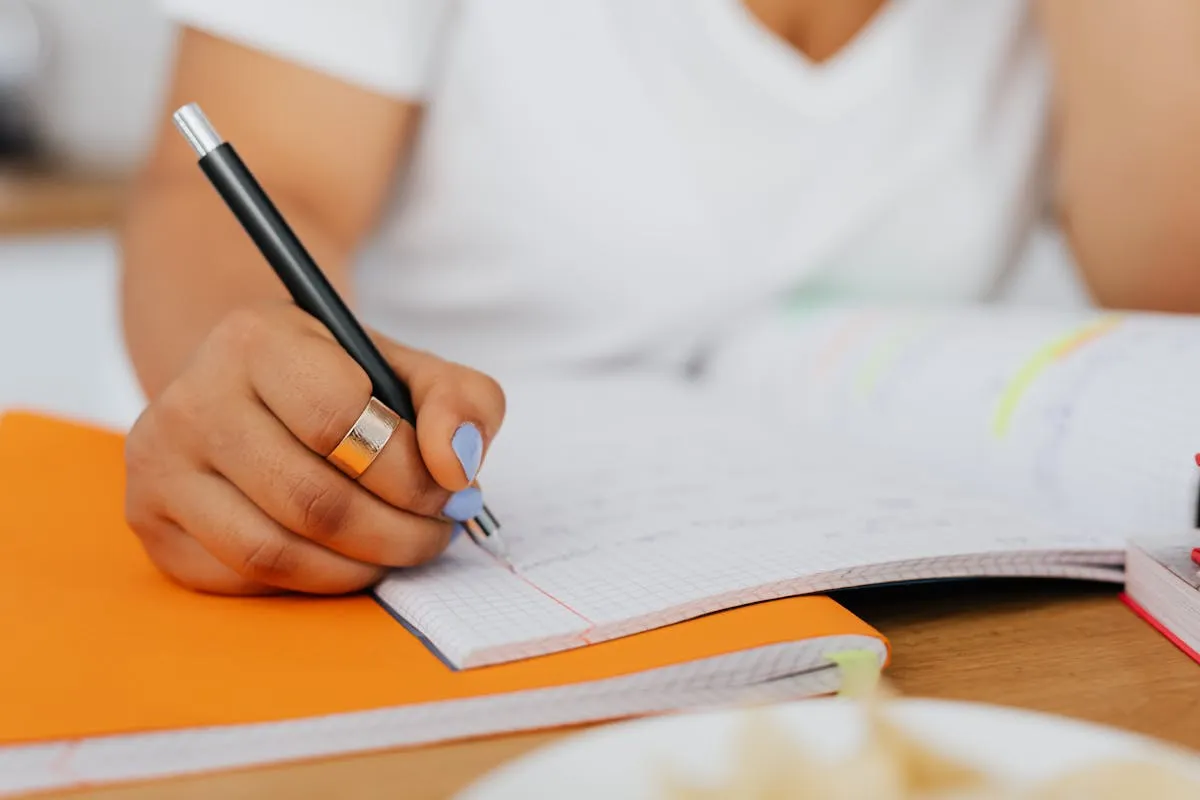 Estudante concentrada escrevendo em caderno com calendário e laptop sobre mesa