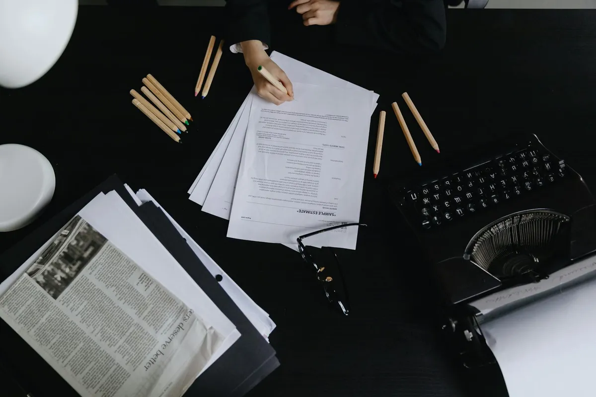Folhas de papel em cima de uma mesa com caneta e caderno, representando formatação de trabalho acadêmico