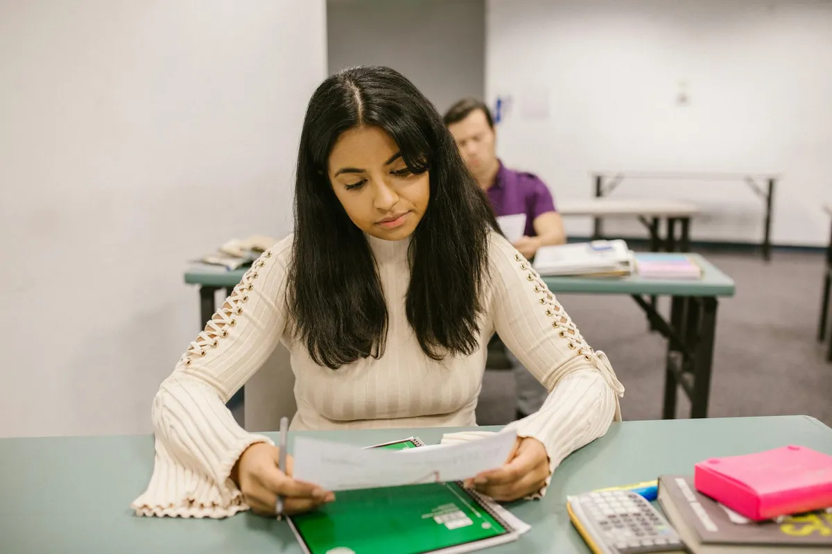 Pessoa revisando documento acadêmico com caneta vermelha sobre mesa de estudos