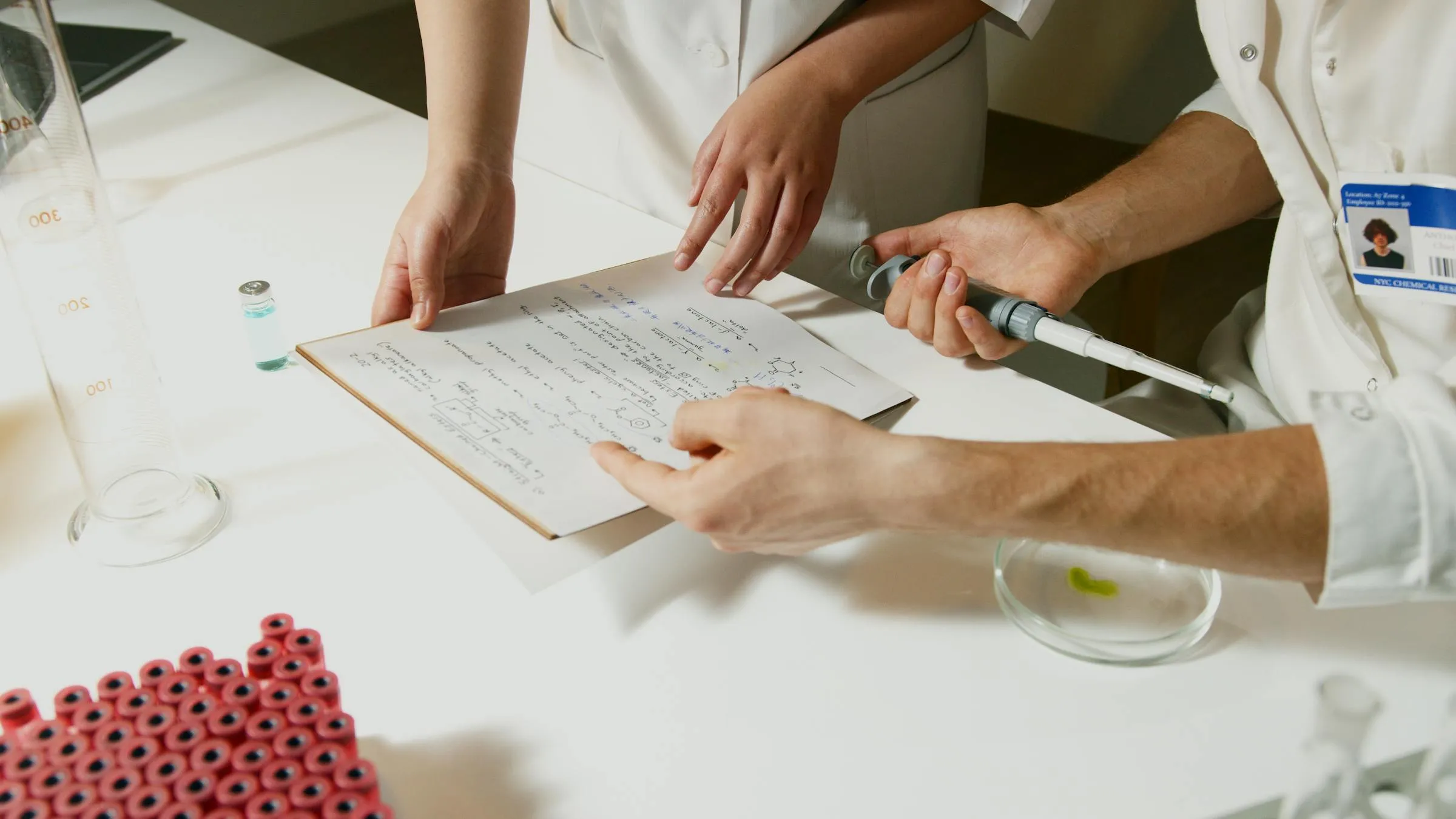 Pesquisadora lendo documentos de editais em mesa de trabalho com computador ao fundo