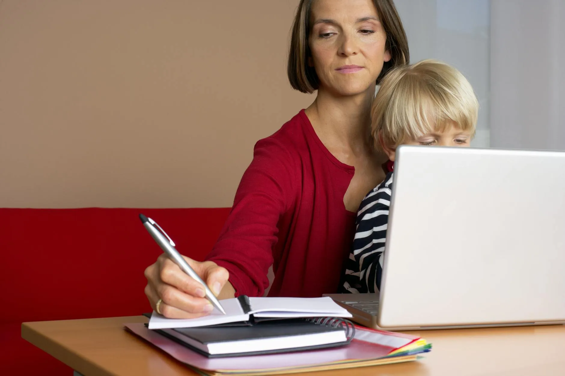 Mulher estudando em casa com laptop enquanto cuida de atividades domésticas ao fundo