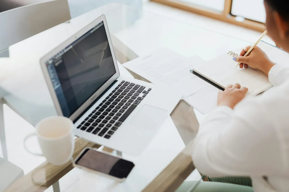 Pesquisador escrevendo em laptop com documentos organizados ao redor, representando produtividade acadêmica