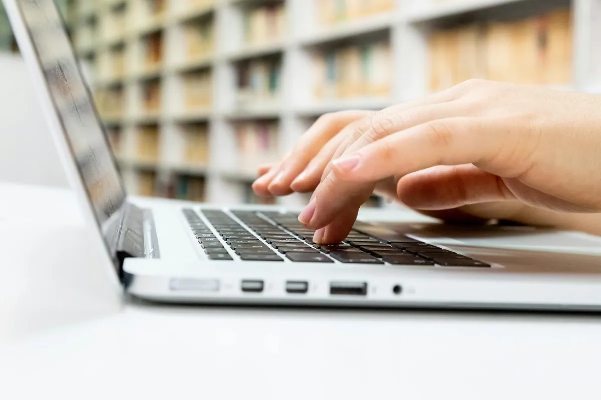 Tela de computador com busca acadêmica aberta ao lado de caderno de anotações