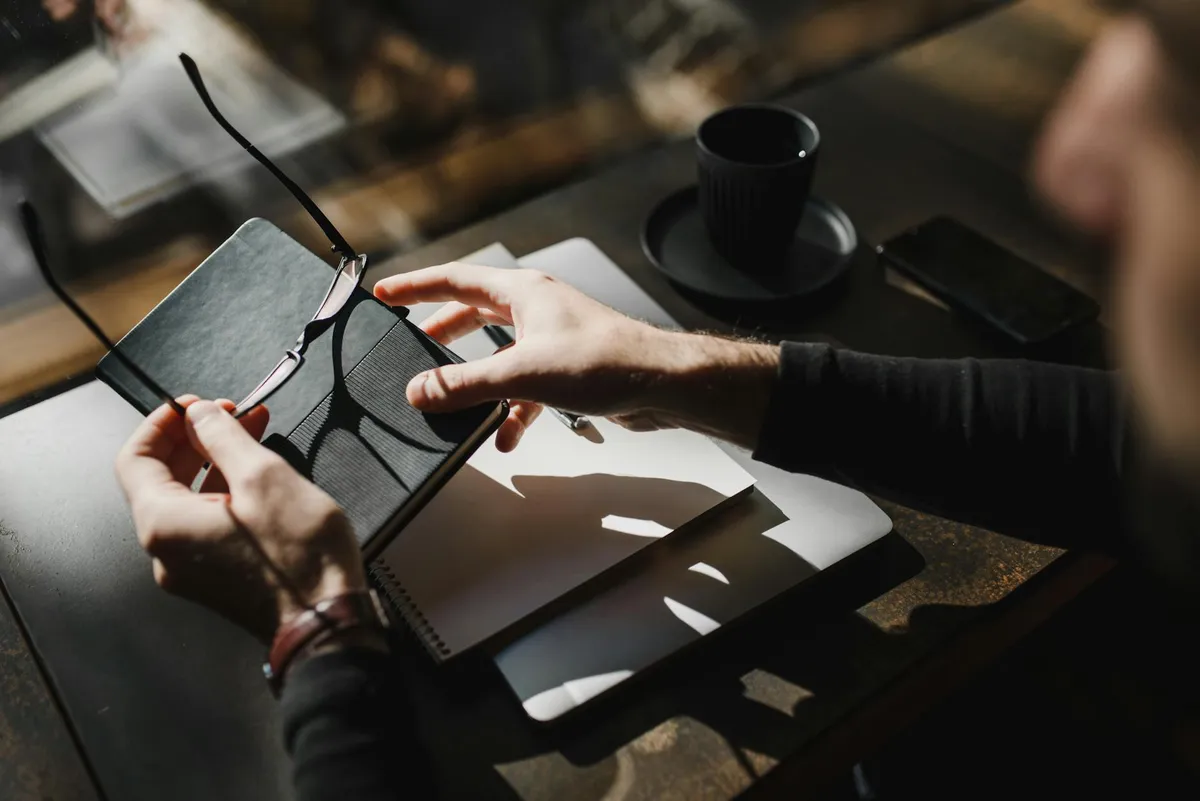 Pesquisadora escrevendo em caderno com documentos acadêmicos ao redor, refletindo sobre sua trajetória