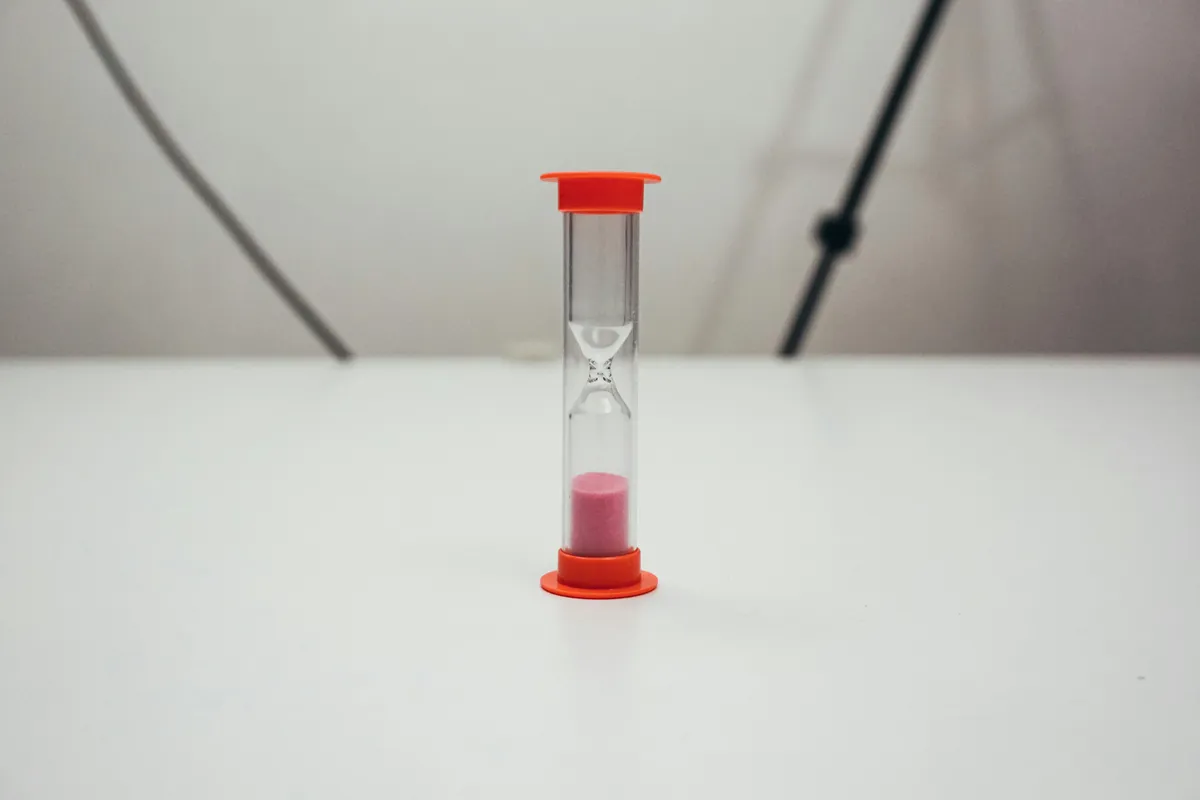 Relógio de areia sobre mesa com cadernos e caneta, simbolizando o tempo na pesquisa