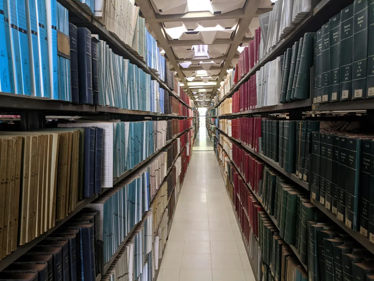 Vista em perspectiva de corredor de biblioteca com estantes coloridas repletas de livros