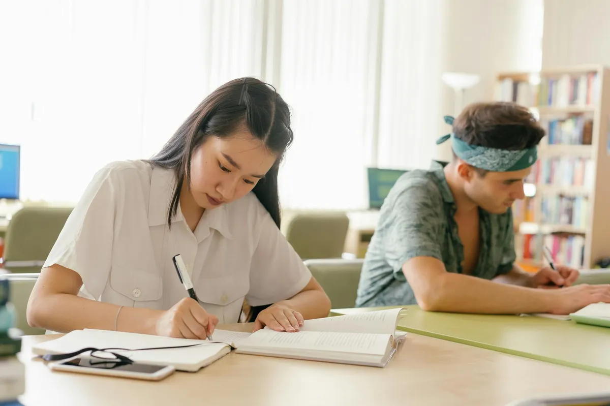 Estudante lendo documento com anotações em mesa de biblioteca universitária