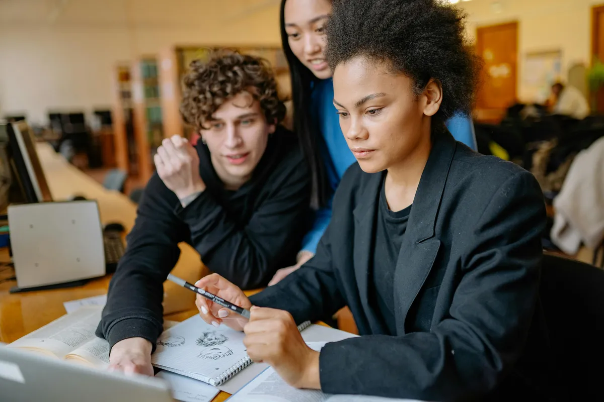 Grupo de estudantes colaborando em torno de uma mesa com papéis e laptops