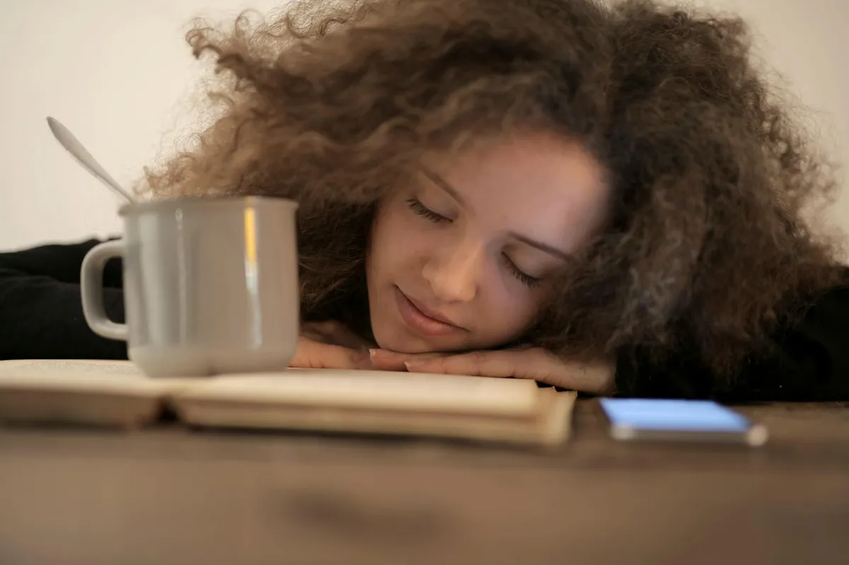 Pessoa descansando com xícara de café perto de livros e caderno