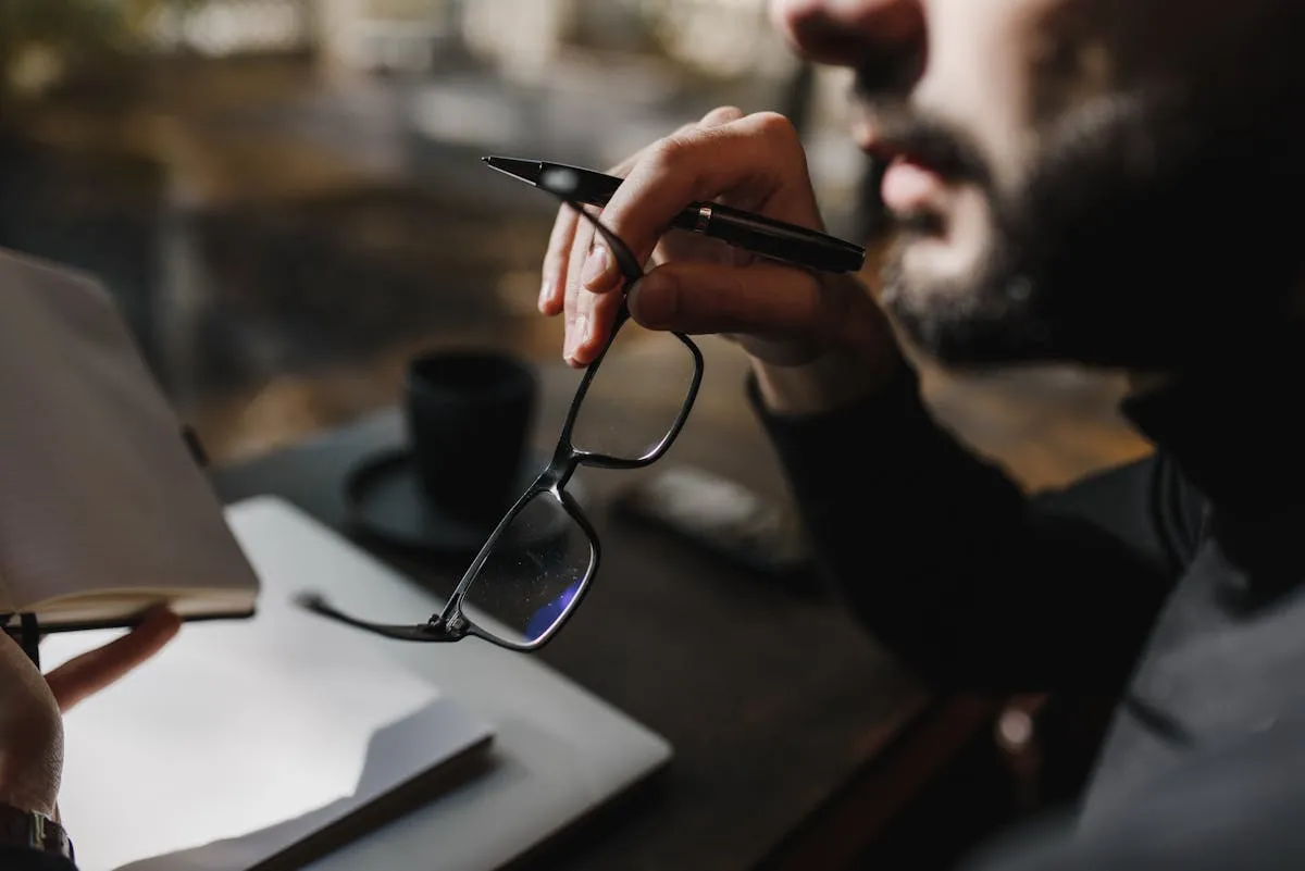 Pessoa sentada em posição reflexiva perto de janela, luz natural ao fundo, em ambiente de estudo