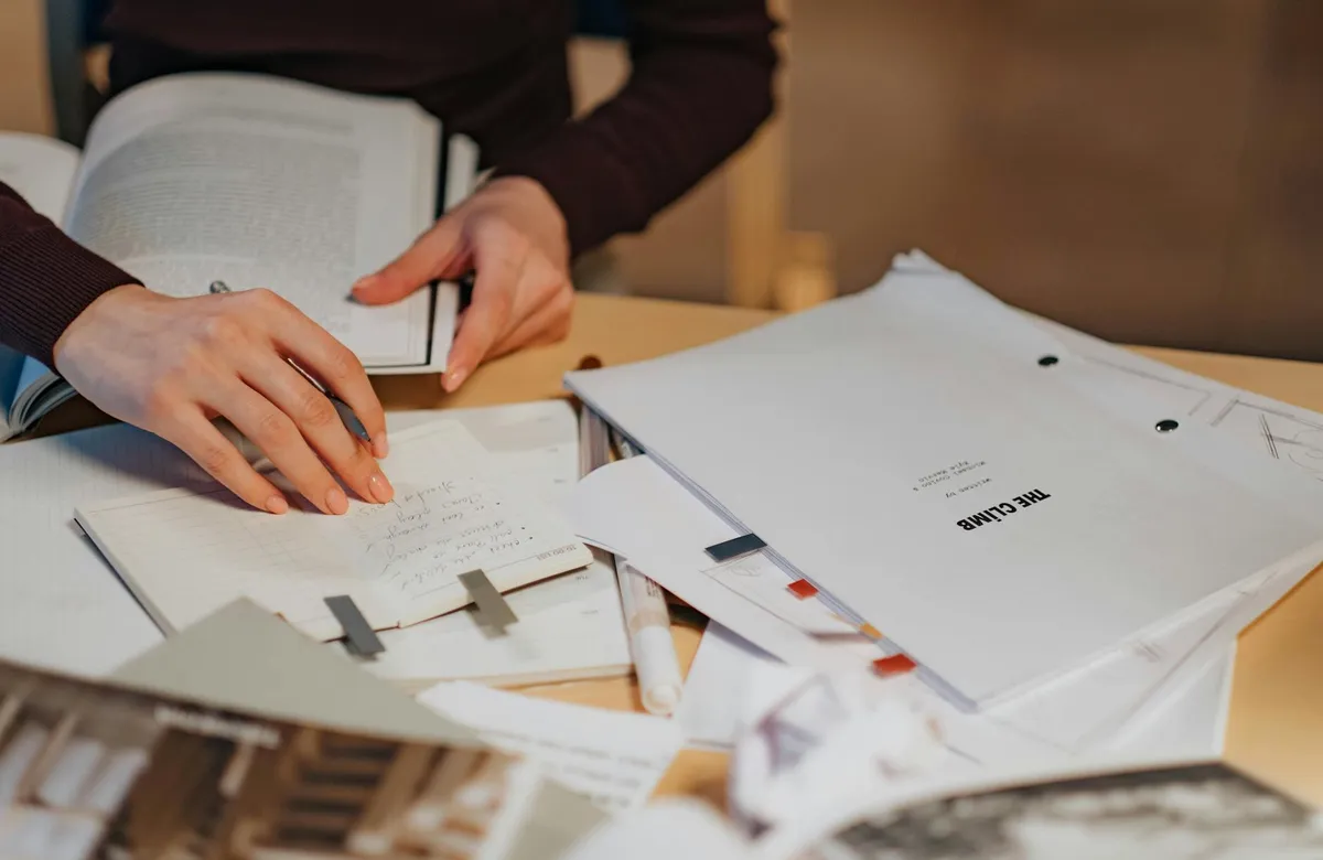 Pesquisadora lendo documentos em mesa de trabalho com caderno de anotações
