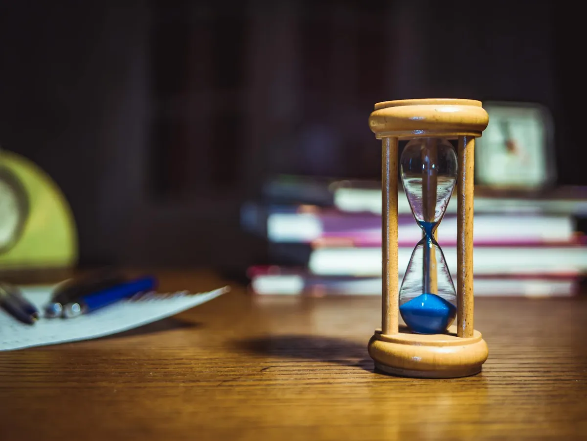 Mesa de estudos com livros, caderno e relógio visível, ambiente organizado para trabalho acadêmico