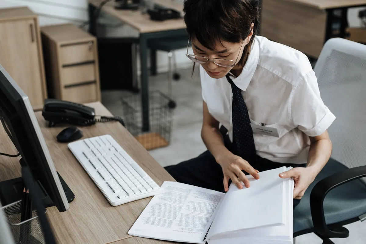 Pesquisadora lendo documento oficial em mesa com computador e papéis de pesquisa