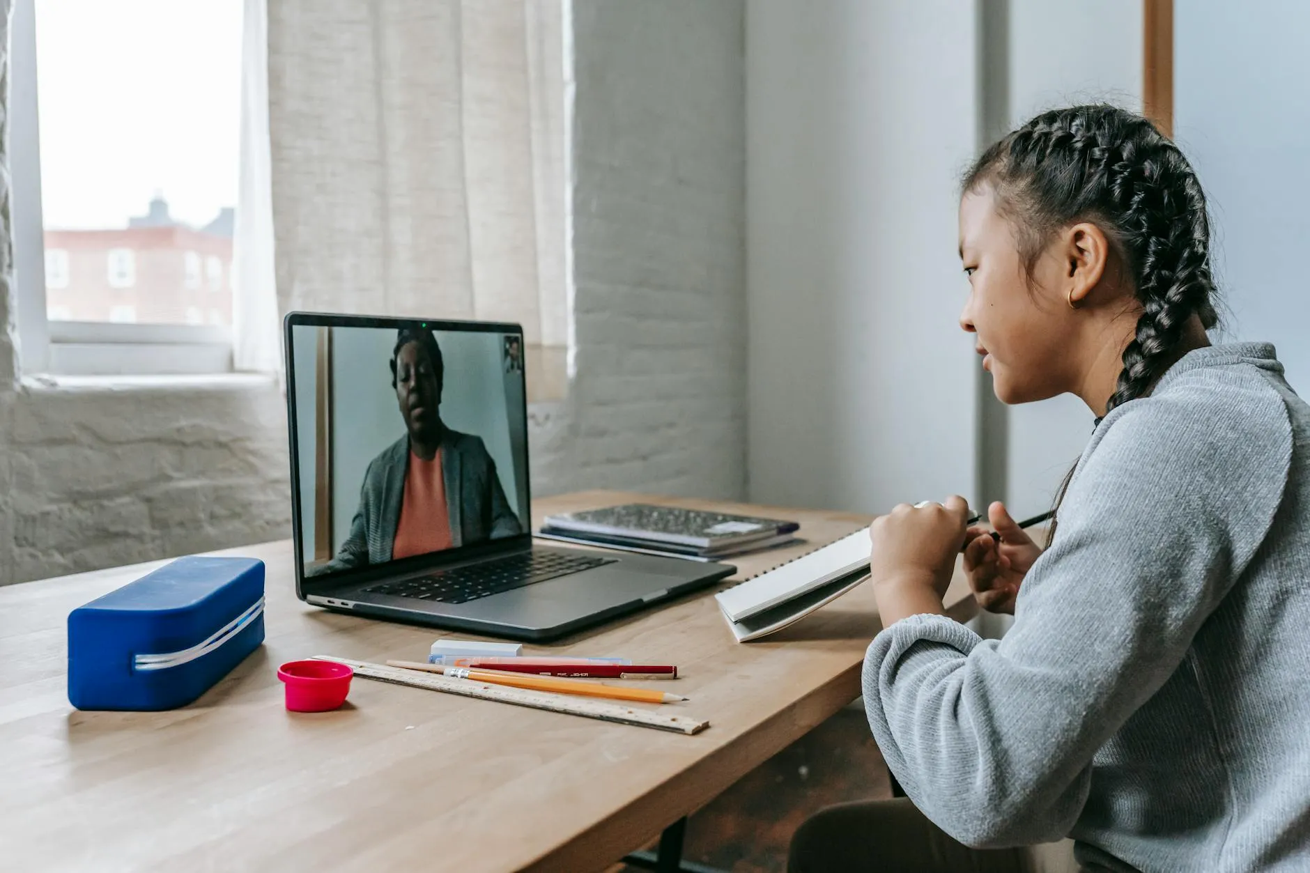 Pessoa estudando em notebook em casa com caderno de anotações