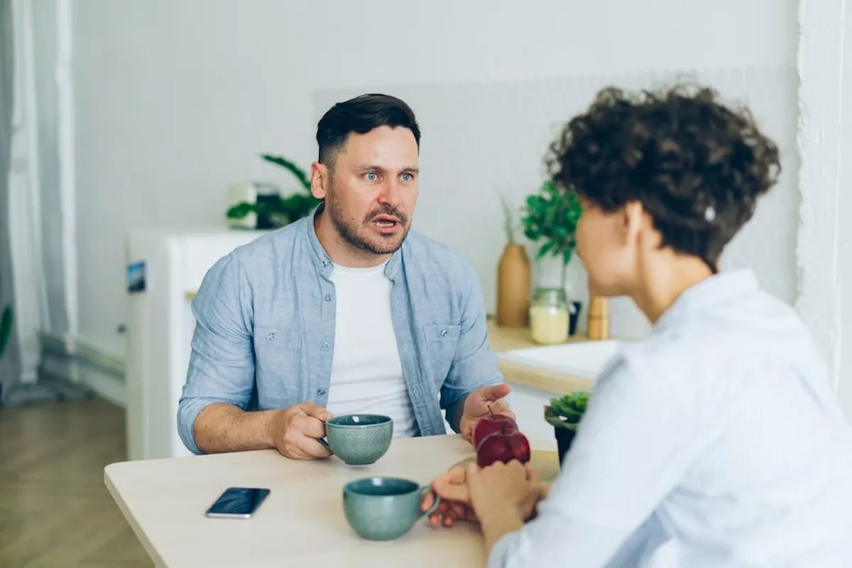 Casal conversando à mesa com computador e livros ao fundo