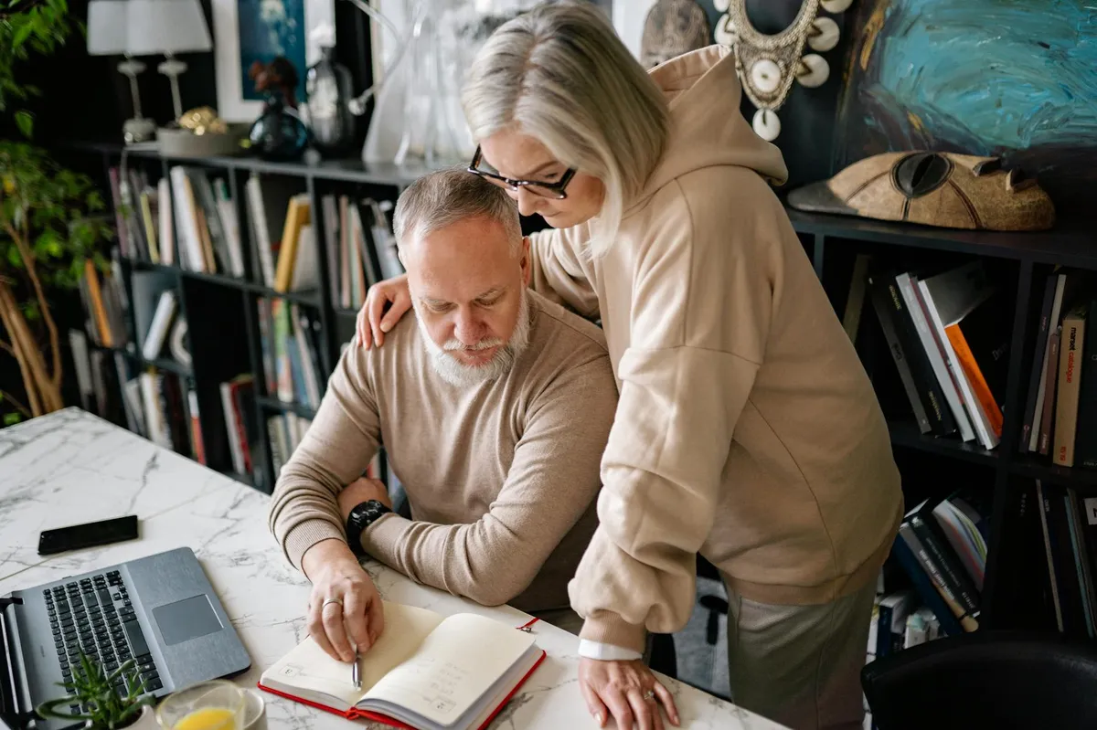 Casal conversando em casa enquanto uma pessoa tem livros de pós-graduação sobre a mesa