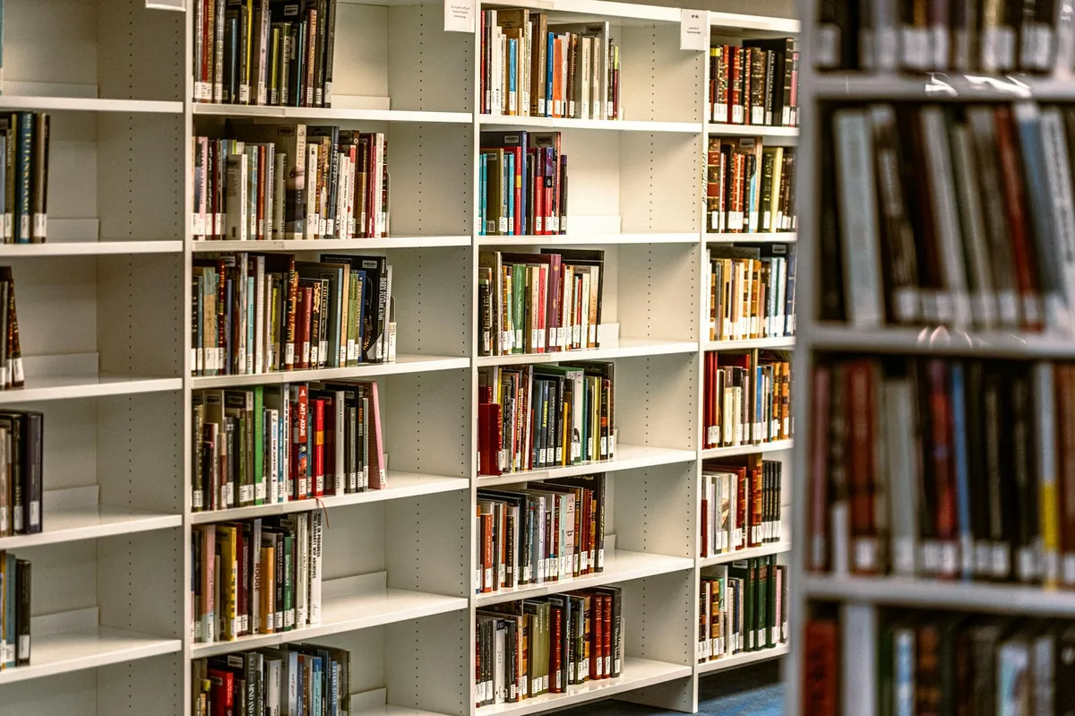 Estante com livros acadêmicos variados em biblioteca universitária