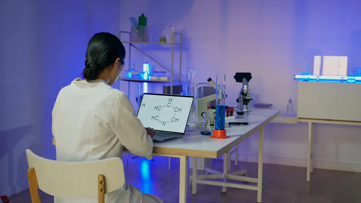 Pesquisadora escrevendo artigo científico em laptop com anotações ao redor