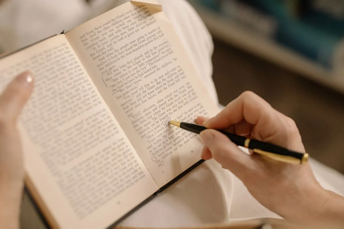 Pessoa lendo livro com caneta e caderno de anotações ao lado