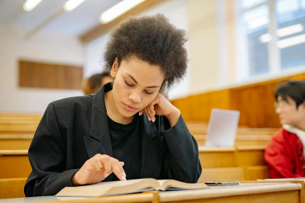 Estudante de pós-graduação com expressão de ansiedade olhando para livros e papéis na mesa