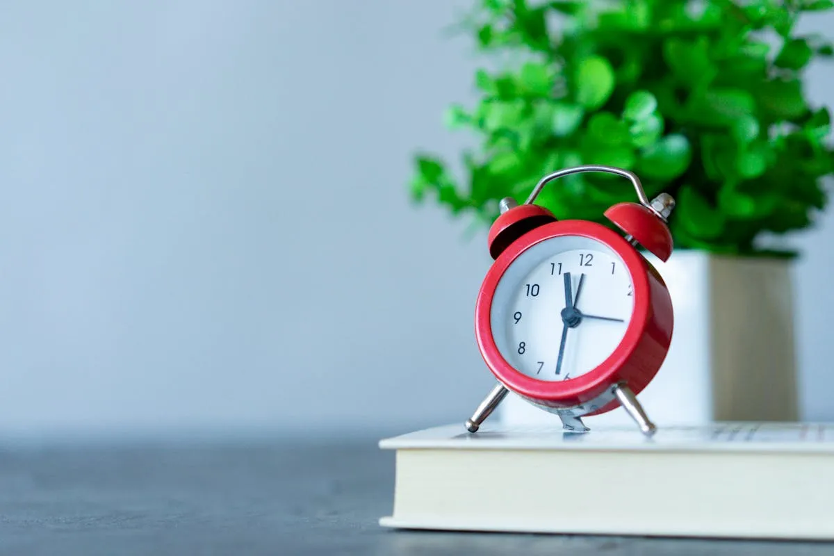 Relógio de cozinha vermelho sobre mesa de trabalho com cadernos e canetas