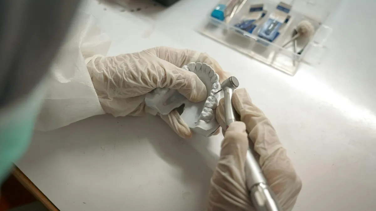 Dentista moldando prótese dentária com ferramentas de precisão e luvas