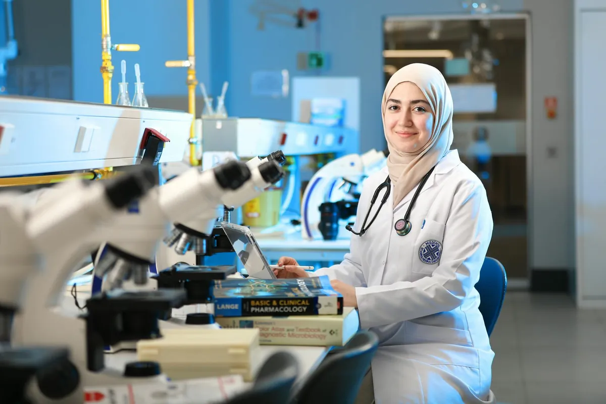 Pesquisadora em laboratório consultando livros de referência ao lado de microscópios