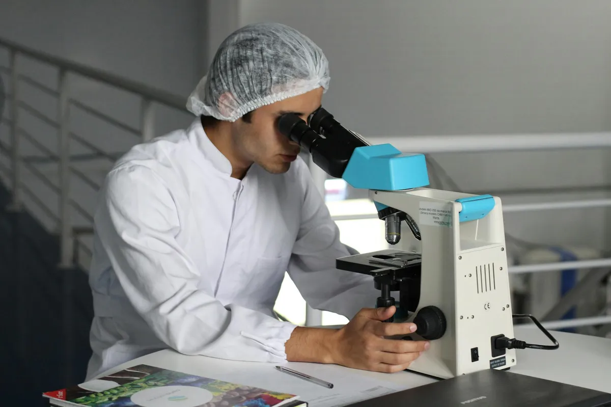 Cientista de jaleco usando um microscópio em pesquisa na área da saúde